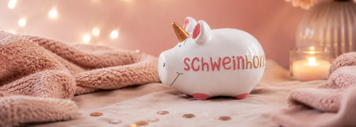 Sparschwein "Schweinhorn" vor einem rosanem Hintergund mit Licherketten und kerzenschein