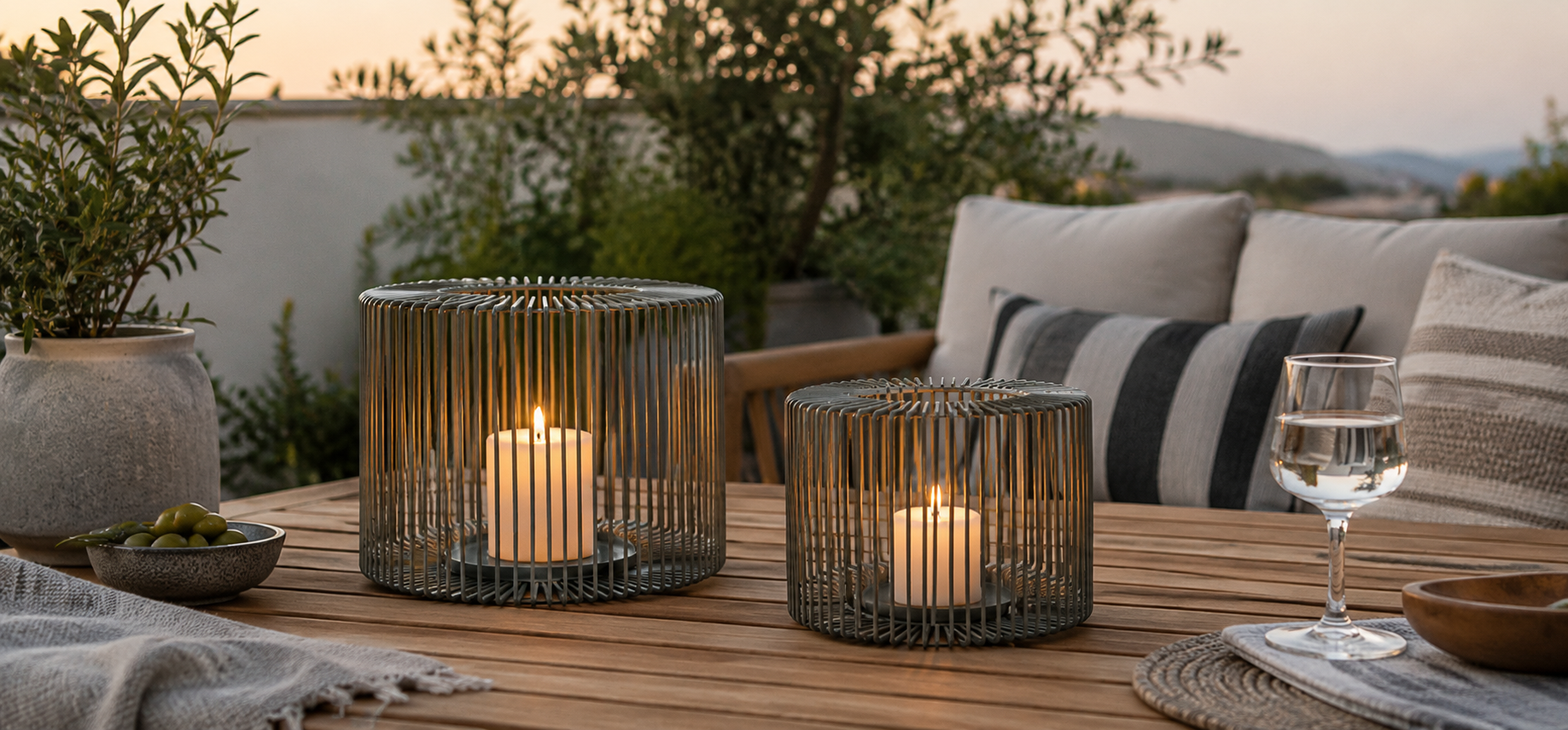zwei moderne windlichter auf einer gemütlichen Terasse im wunderschönem abendlichen Sonnenlicht, gemütliche Sommerliche einrichtung mit Kissen, Holztisch und schöner Tischdekoration