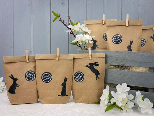 Drei braune Wundertüten mit einem Aufkleber auf dem steht "Frohe Ostern" mit drei verschiedenen Hasen Muster in Schwarz