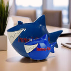 2 Dunkelblaue Haie, Sparschweine aus Keramik in Hai Form, großes Weißes Gebiss, lustige 3D Augen, rote 3D Aufschrift auf der Seite: Immo-Hai, von der rechten Seite fotografiert, Großer und Kleiner Hai vor einander, hintergrund Büro verschwommen/unfokussie