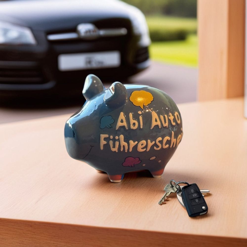 Grau Blaues Sparschwein aus Keramik, 9 x 9 x 12,5 cm, neon orange Details (Schweinohren & Füße), zweier Schriftzug "Abi Auto Führerschein", Denkblasen in gelb, blau und rosa, Gesichtzüge in Schwarz, fotografiert auf einem Holztisch mit Autoschlüssel, Auto