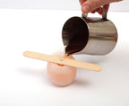 Jemand gießt das Wachs in die Gußform während das Holz Stäbchen den Docht in Mittlere Position hält