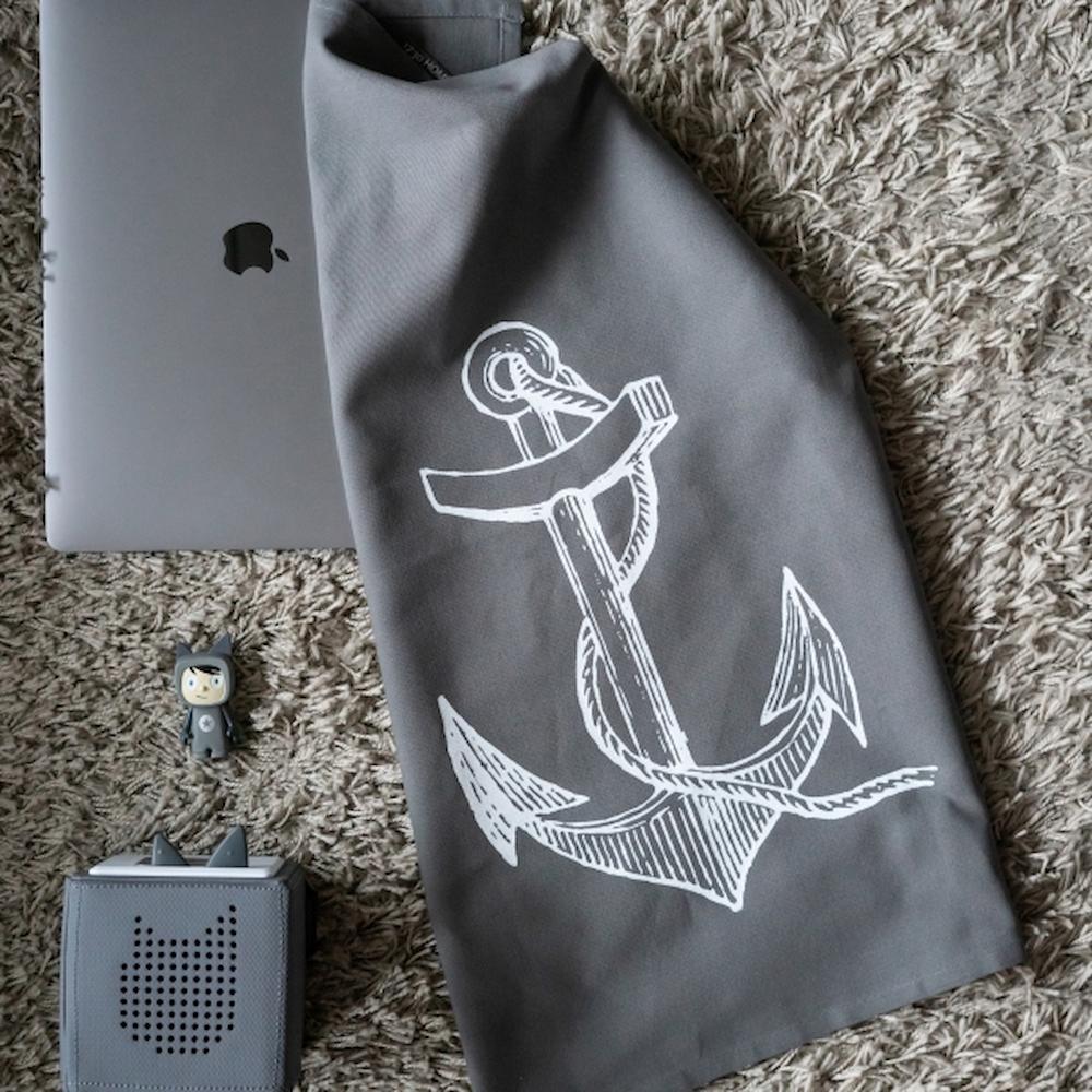 Graues Baumwoll-Geschirrtuch mit einem weißen Anker-Aufdruck hängt in der Küche mit Deko