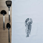 Das Hummer-Geschirrtuch zusammen mit Küchenutensilien aus Edelstahl