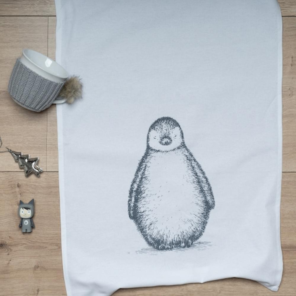 Das Pinguin-Geschirrtuch auf einem Tisch zusammen mit einer grauen Tasse und Deko