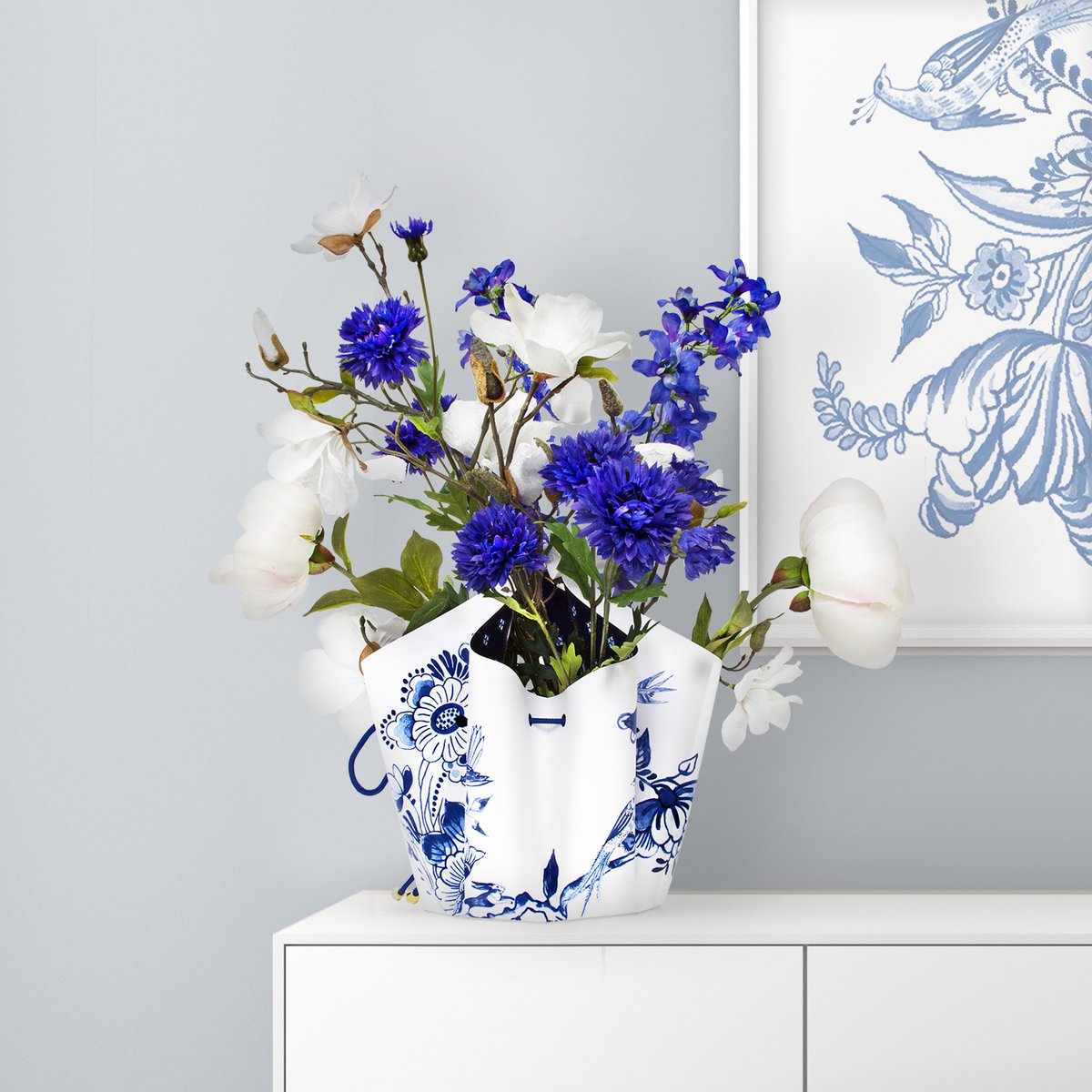 Die Faltvase mit einem Delfter Blau Design in Blau/Weiß, auf einem Tisch mit bluen Blumen 