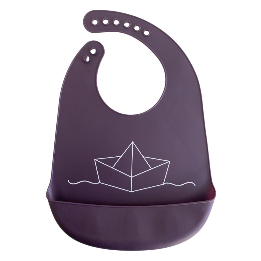 Lila Silikon Lätzchen mit einem aufgedruckten schwimmenden weißen Papierboot und einer Auffangschale