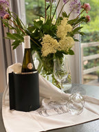 Weinkühler in schwarzer Ledermanschette auf einem gedeckten Tisch, zusammen mit einer Weinflasche und Weingläsern