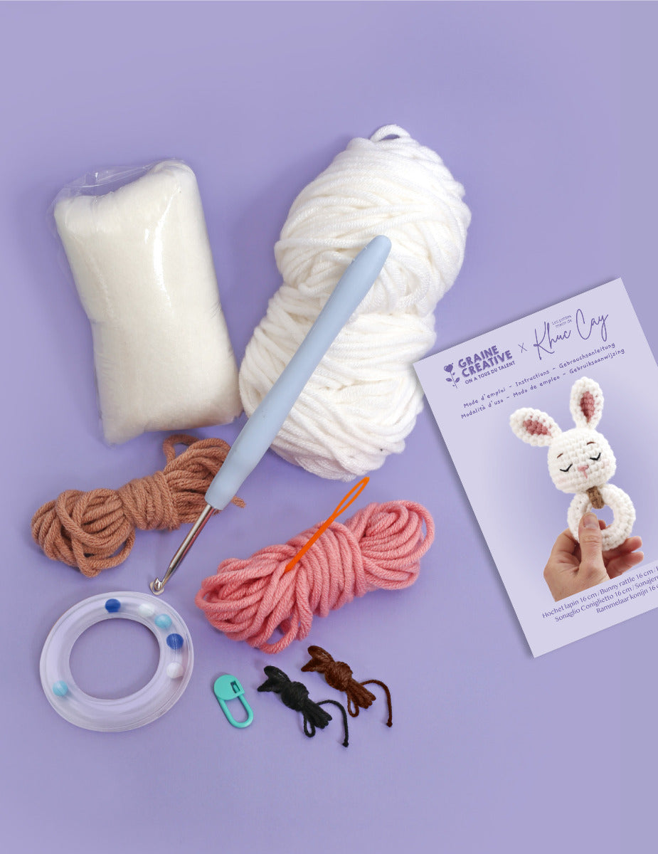 Die Rohmaterialien Baumwolle, Füllmaterial Häckelnaden und Ring mit Rasseleffekt samt Anleitung für den Kaninchen Plüsch-Greifring für Babys