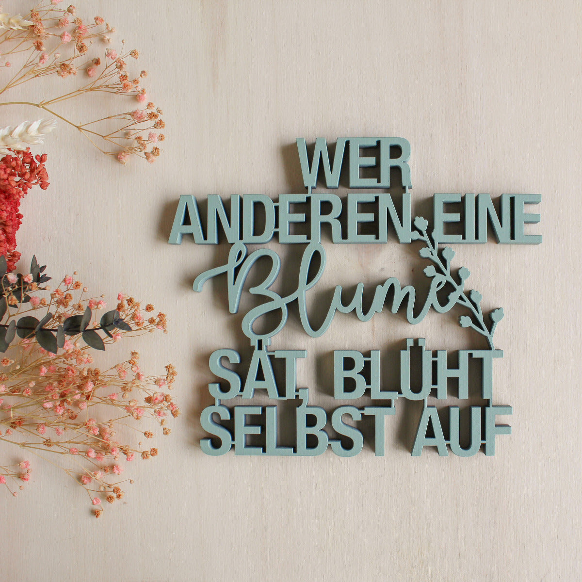 Türkiser Dekorations Holzschriftzug mit dem Text "Wer anderen eine Blume sät, blüht selbst auf"