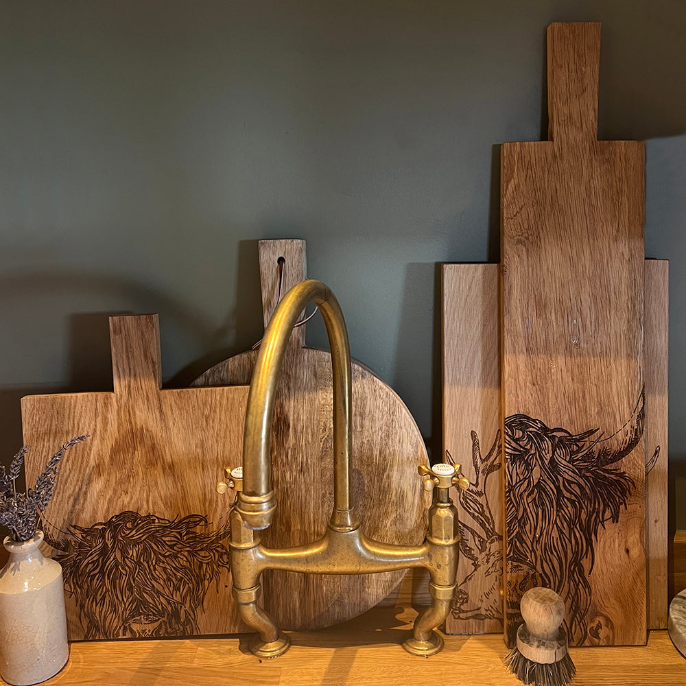 Ein Eichen Servierbrett mit einem eingebranntem "Hochlandrind" Design auf einem Tisch mit anderen Brettern