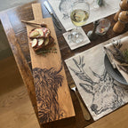 Ein Eichen Servierbrett mit einem eingebranntem "Hochlandrind" Design auf einem Tisch