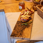 Ein Eichen Servierbrett mit einem eingebranntem "Hochlandrind" Design auf einem Tisch mit Serviertem Brot und Pfirsichscheiben