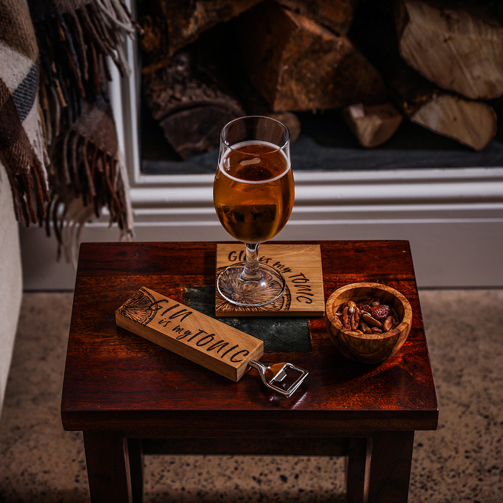 Ein Eichen Flaschenöffner mit einem eingebrannten Limonetten-Design und der Schrift "GIN is my TONIC" auf einem Tisch mit einem fertig gemischten Glas, dass auf einem Absetzter ebenfalls im GIN TONIC design steht