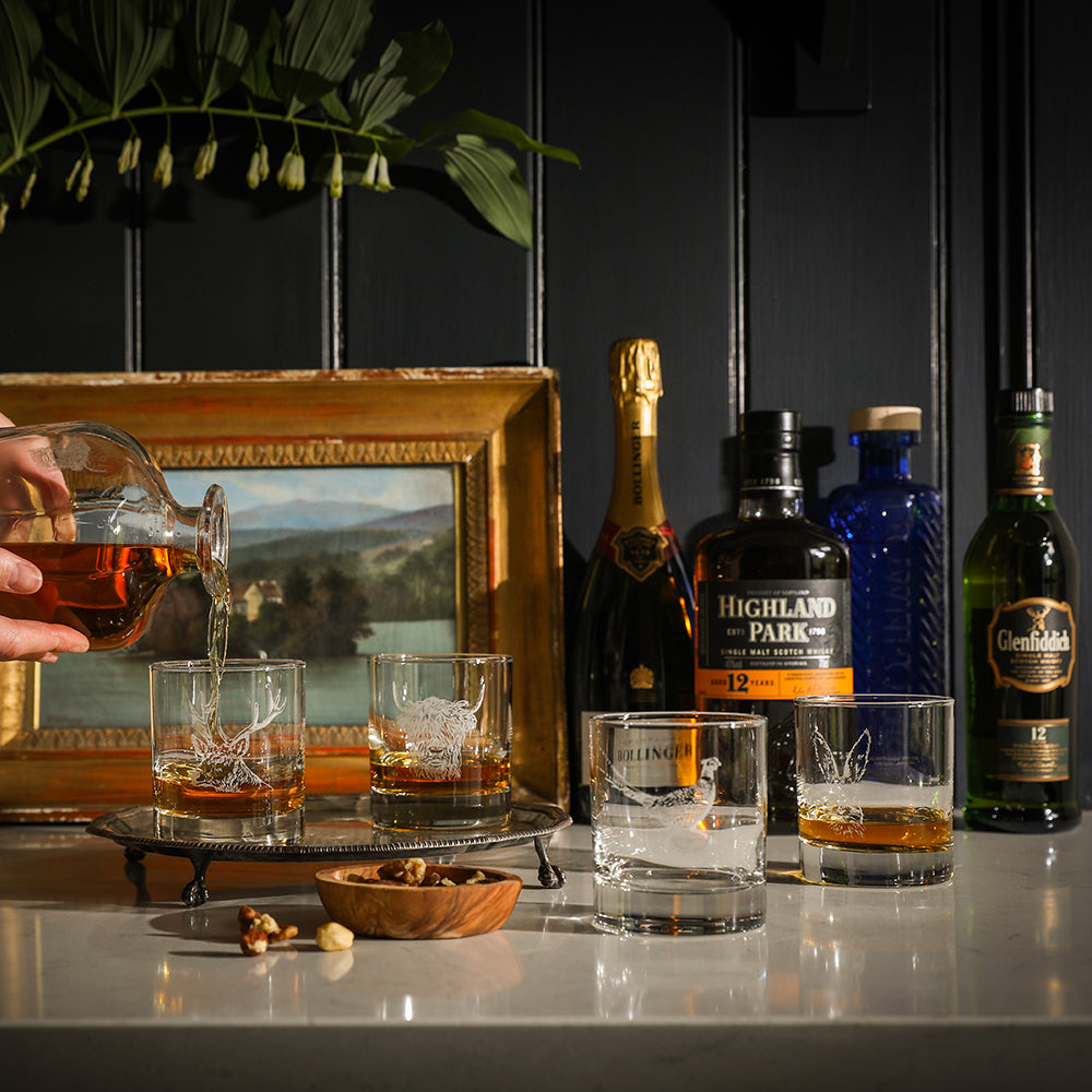 Zwei Whisky-Gläser mit aufgedruckten "Hochlandrind" Design, auf einem Tisch in dem Whisky gefüllt ist.