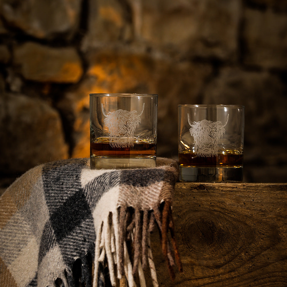 Zwei Whisky-Gläser mit aufgedruckten "Hochlandrind" Design, auf einem Tisch in dem Whisky gefüllt ist