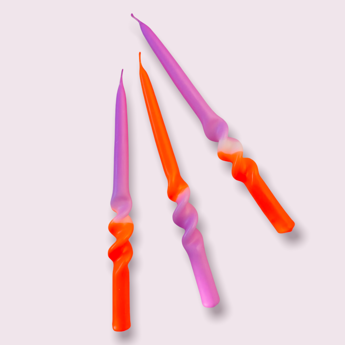 Drei Stabkerzen in den Farben Lila und Orange, die Kerzen haben in der unteren Hälfte eine Spirale Form