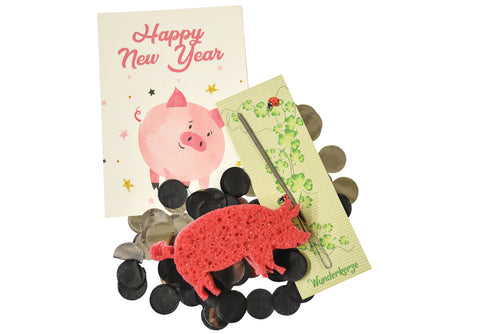 Eine Postkarte mit einem Schwein und der Schrift "Happy New Year", ein Schwamm in Schweine-Form, eine in Glücksverpackung eingepackte Wunderkerze und Stoff-Konfetti zum werfen