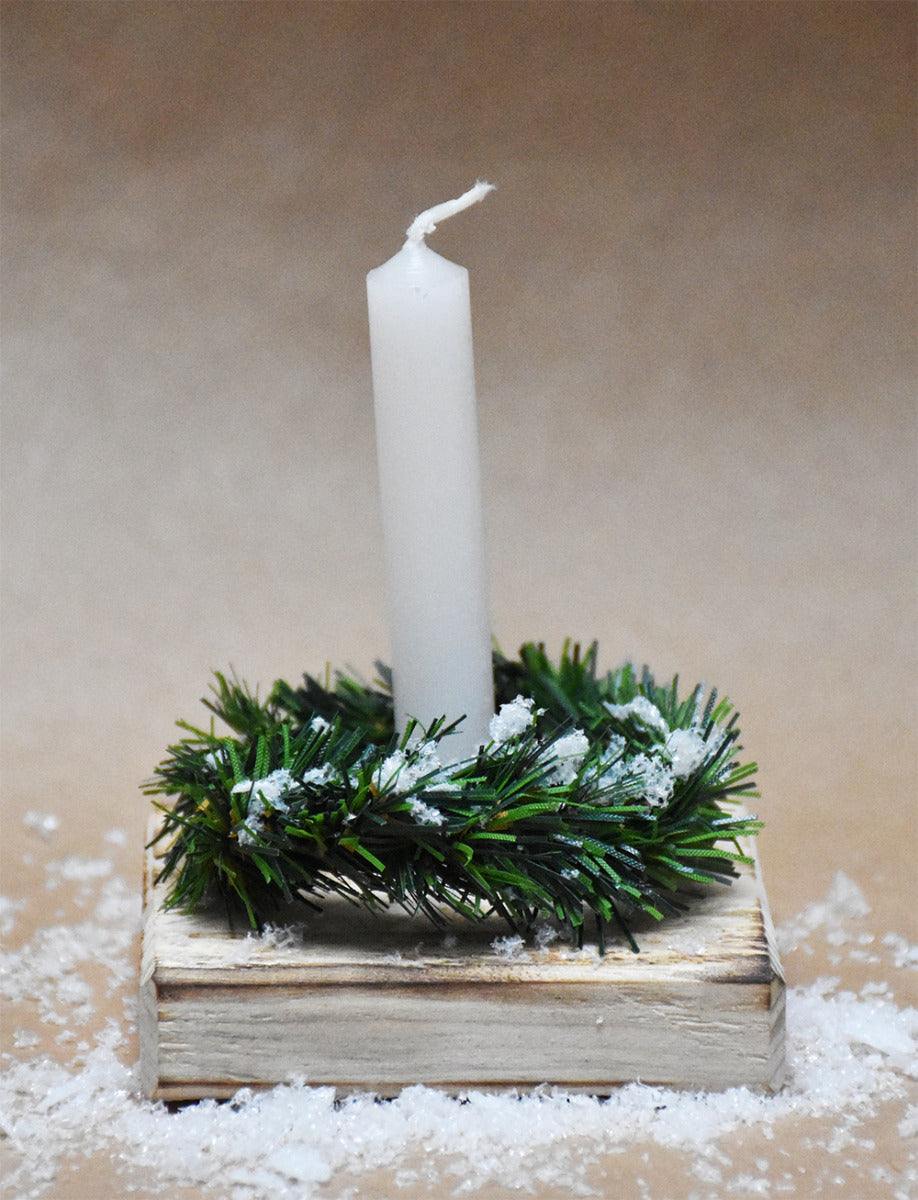 Weihnachtslicht to go mit einer kleinen  Quadratischen Holzplatte auf der ein Kunststoffkranz liegt und in der Mitte eine weiße Stabkerze steckt