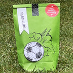 Grüne Wundertüte "Für Fußball Fans" steht auf einem Fußballfeld mit aufgedrucktem Fußball Motiv
