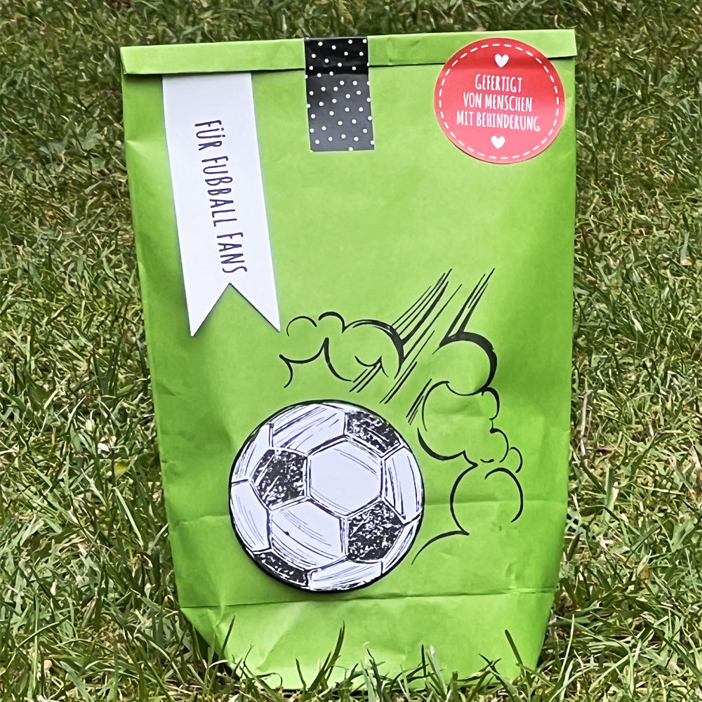 Grüne Wundertüte "Für Fußball Fans" steht auf einem Fußballfeld mit aufgedrucktem Fußball Motiv