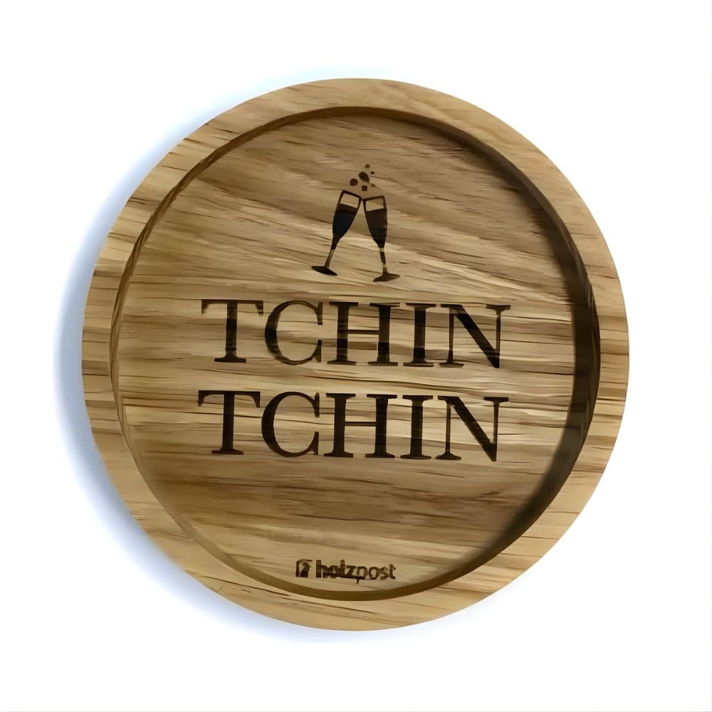 Eingekerbter Holzuntersetzer mit dem aufgedruckten Spruch „TCHIN TCHIN" und zwei kleinen Sekt-Gläsern