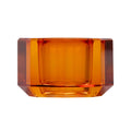 Ein kleiner Kerzenhalter aus Glas in Bernstein Kristall-Optik, bestehend aus mehreren geometrischen Flächen. Der Kerzenhalter hat eine moderne, facettierte Optik, die das Licht reflektiert