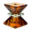 Ein hoher wendbarer Kerzenhalter aus Glas in Braun und Olive Kristall-Optik, bestehend aus mehreren geometrischen Flächen. Der Kerzenhalter hat eine moderne, facettierte Optik, die das Licht reflektiert