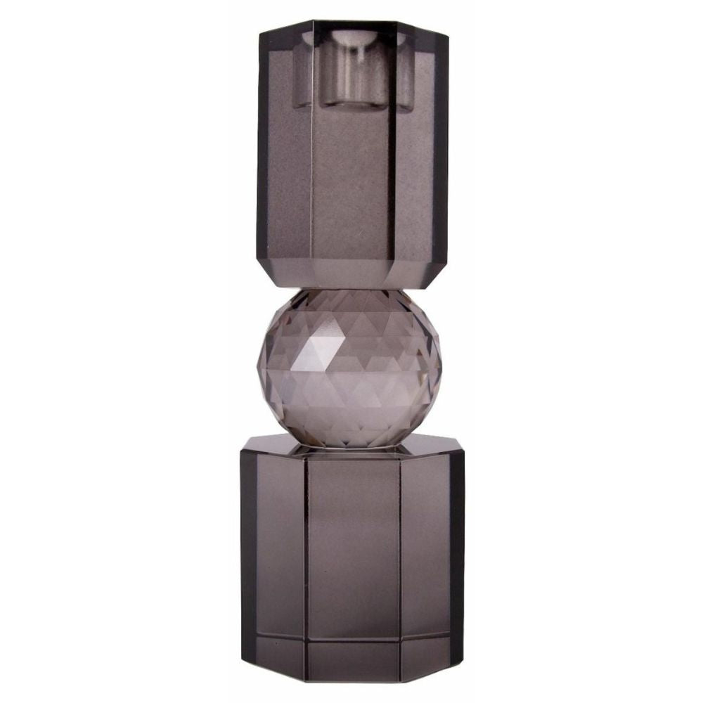 Ein hoher Kerzenhalter aus Glas in Rauchgrauer Kristall-Optik, bestehend aus mehreren geometrischen Flächen. Der Kerzenhalter hat eine moderne, facettierte Optik, die das Licht reflektiert.