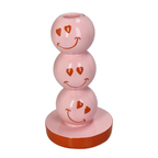 Pinker Kerzenständer aus drei gestapelten kugeln auf denen rote smileys mit Herz förmigen Augen sind