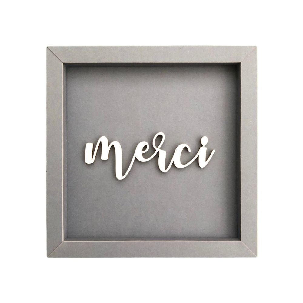 Quadratischer Papp-Bilderrahmen in Dunkelgrau mit der Schrift "Merci"