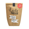 Braune Wundertüte auf der Steht "Gute Reise" mit einem angeklebten Holzstock Wegweiser mit zwei Schildern "Urlaubs Glück" und "Abenteuer Lust"