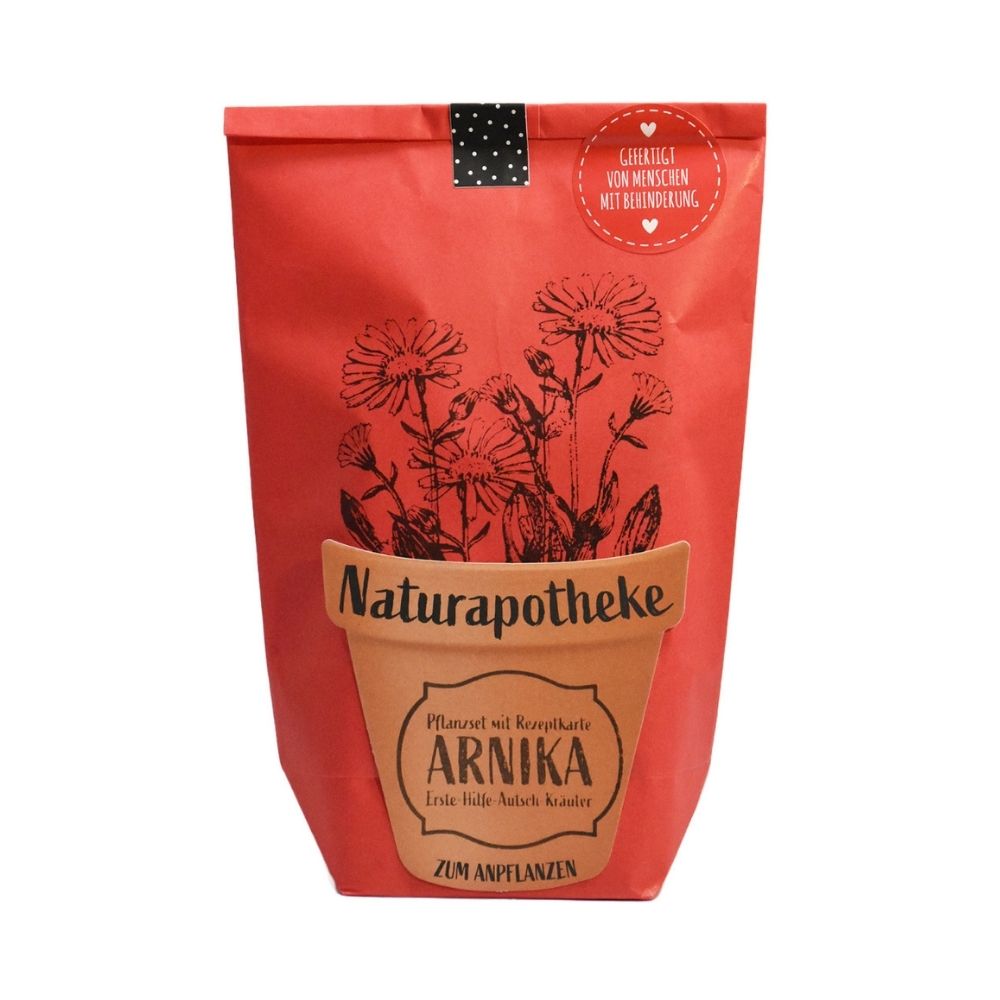 Rote Wundertüte mit einem aufgeklebten Topf auf dem "Naturaphotheke Pflanzset ARNIKA" steht. Aus dem Topf sind aufgedruckte Blumen