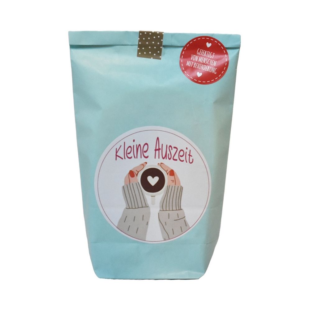 Blaue Wundertüte mit einem Aufdruck von zwei händen, die sich an einer Tasse Kaffee wärmen mit der roten Schrift "kleine Auszeit"