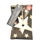 Eine Wundertüte aus Geschenkpapier mit einem Stoffanhänger auf dem Steht "MERRY CHRISTMAS" und einem angehangenen Holz-Sternchen
