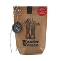 Braune Wundertüte mit einem schwarzen Aufdruck von zwei Kräuterbeuteln und der Schrift "Wander Woman", Oben links ist ein Kompass and einer Kette befestigt