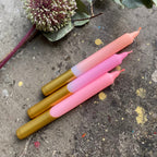 Drei Stabkerzen liegen auf einem Steinernen untergrund mit einer Blume daneben