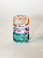 Ein hoher wendbarer Dioptrics Kerzenhalter aus Glas in Petrol, Violett und Pfirsich Kristall-Optik, bestehend aus mehreren geometrischen Flächen. Der Kerzenhalter hat eine moderne, facettierte Optik, die das Licht reflektiert