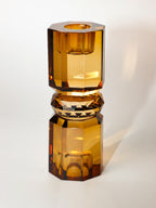 Ein hoher wendbarer Kerzenhalter aus Glas in Brauner Kristall-Optik, bestehend aus mehreren geometrischen Flächen. Der Kerzenhalter hat eine moderne, facettierte Optik, die das Licht reflektiert.
