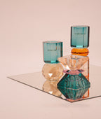 Ein hoher wendbarer Kerzenhalter aus Glas in Petrol, Pink und Pfirsich Kristall-Optik auf einem Spiegel mit anderen Kristallhaltern