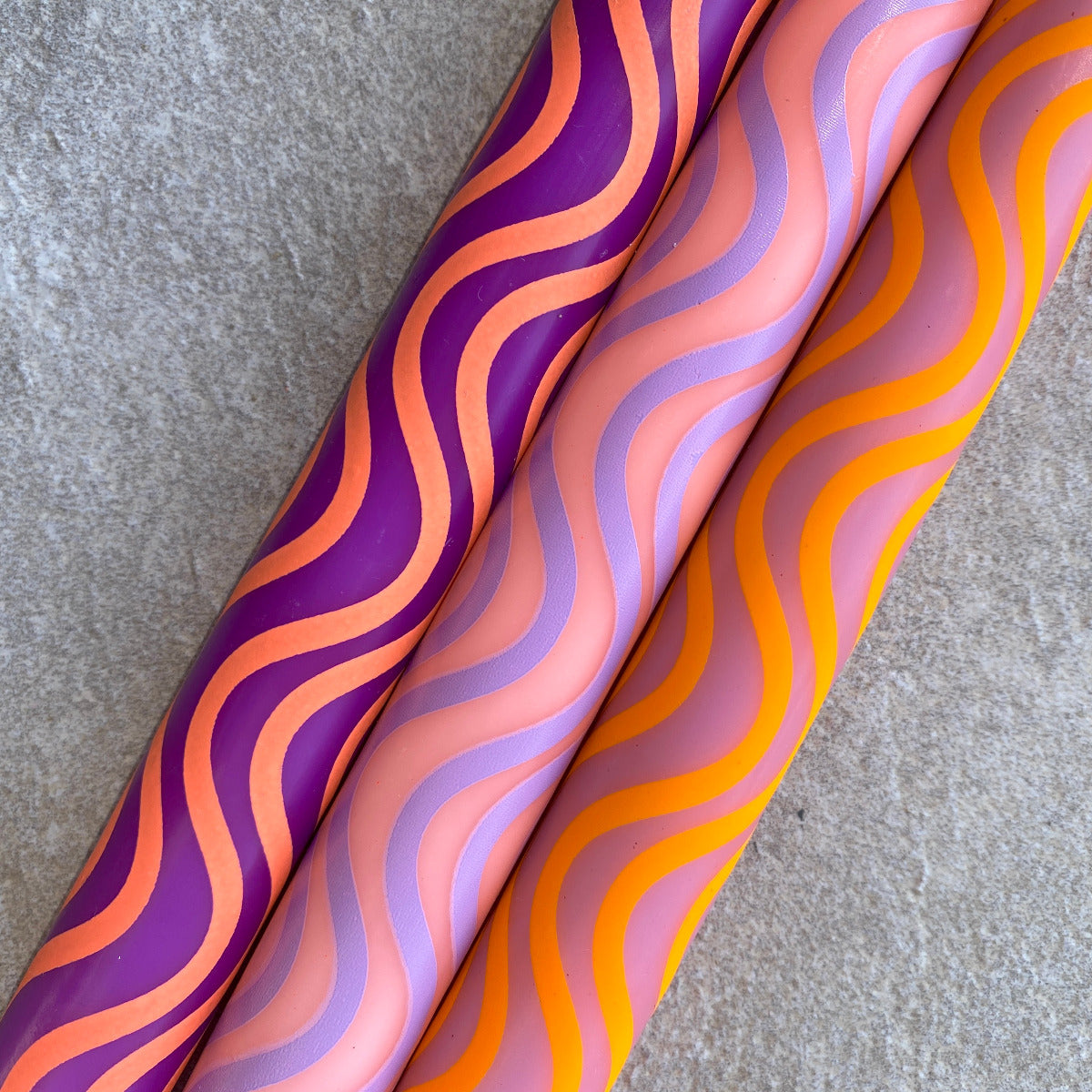 Drei Stabkerzen mit Wellenmusterung in den Farben Lila, Pink, und Orange, Nahaufnahme