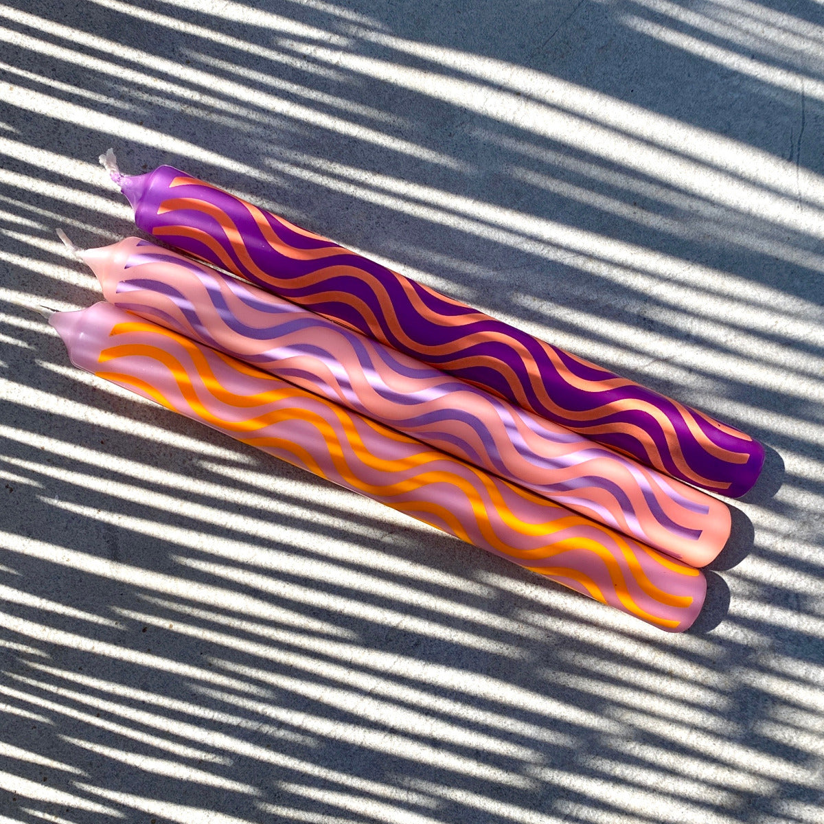 Drei Stabkerzen mit Wellen Musterung in den Farben Lila, Pink, und Orange, Nahaufnahme in der Sonne