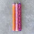 Drei Stabkerzen mit Wellenmusterung in den Farben Lila, Pink, und Orange
