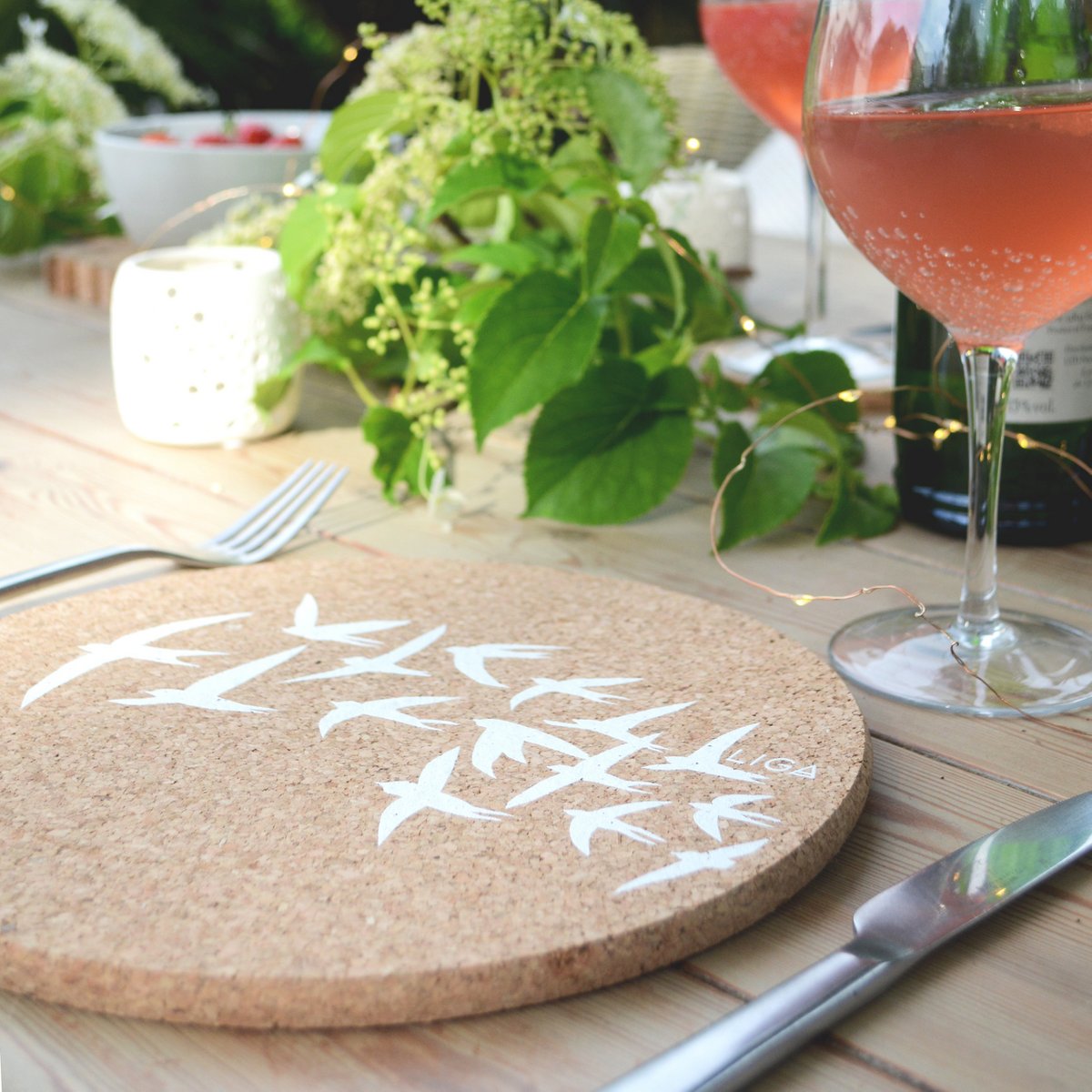 Kork-Tischset mit Schwalben Muster auf einem Tisch mit einem Glas Wein und Pflanzen im Hintergrund