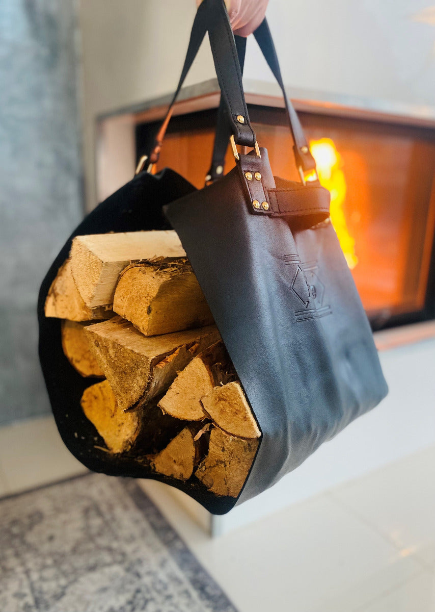 Brennholztragetasche aus Leder in schwarz gefüllt mit Brennholz für den Kamin, Kamin mit Feuer im Hintergrund, gemütliche Atmosphäre, Holzträger wird getragen