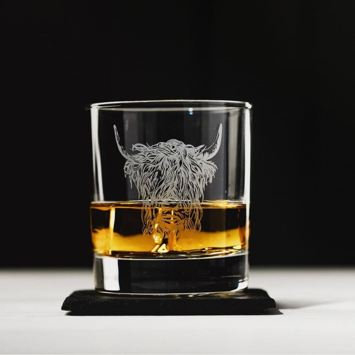 Whisky-Gläs mit aufgedruckten "Hochlandrind" Design, auf einem Tisch in dem Whisky gefüllt ist