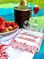 Die Schachtel des Spiels "Liebling - was du schon immer über deinen Partner wissen wolltest" an einem für 2 gedeckten Tisch mit Weingläser und Erdbeeren