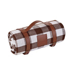 Wasserdichte Picknickdecke eingerollt mit Riemengurten in Lederoptik und Metallschnallen fixiert, Tragegriff um Picknickdecke zu transportieren, braunkarierte Picknickdecke, schräg von der Seite zu sehen