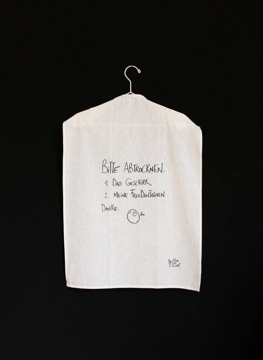 Das weiße Geschirrtuch mit der schwarzen Schrift "Bitte Abtrockenen: 1.Das Geschirr  2.Meine Freudentränen Danke." aufgehangen auf einem Bügel