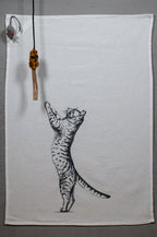 Weißes Geschirrtuch ausgebreitet mit der Katze, die sich nach oben streckt. Und oben links ist eine kleine Maus platziert.